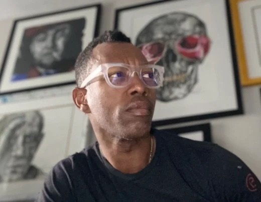 Tee Roy in his studio, artwork on the wall behind him